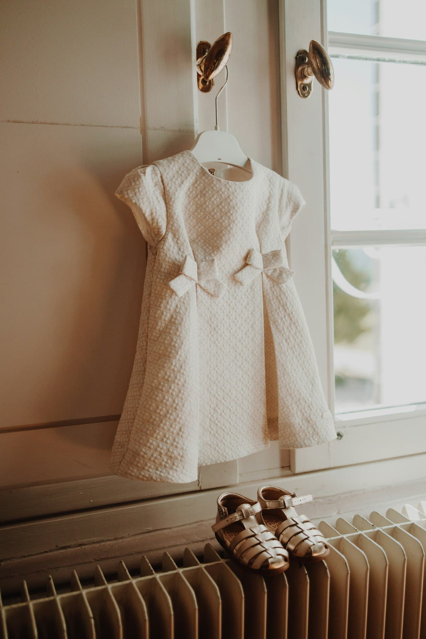 Ivory textured baby dress on a hanger with small leather sandals